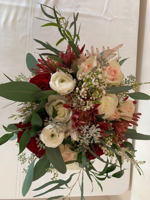 A bouquet of burgundy blooms, peach and white roses, and eucalyptus designed by Elyse Alleman of Plenty of Petals
